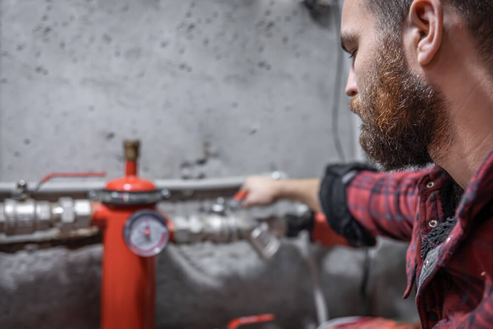 Ein bärtiger Mann im Karohemd stellt in einer Industrieumgebung das Ventil für den hydraulischen Abgleich neben einem roten Manometer ein