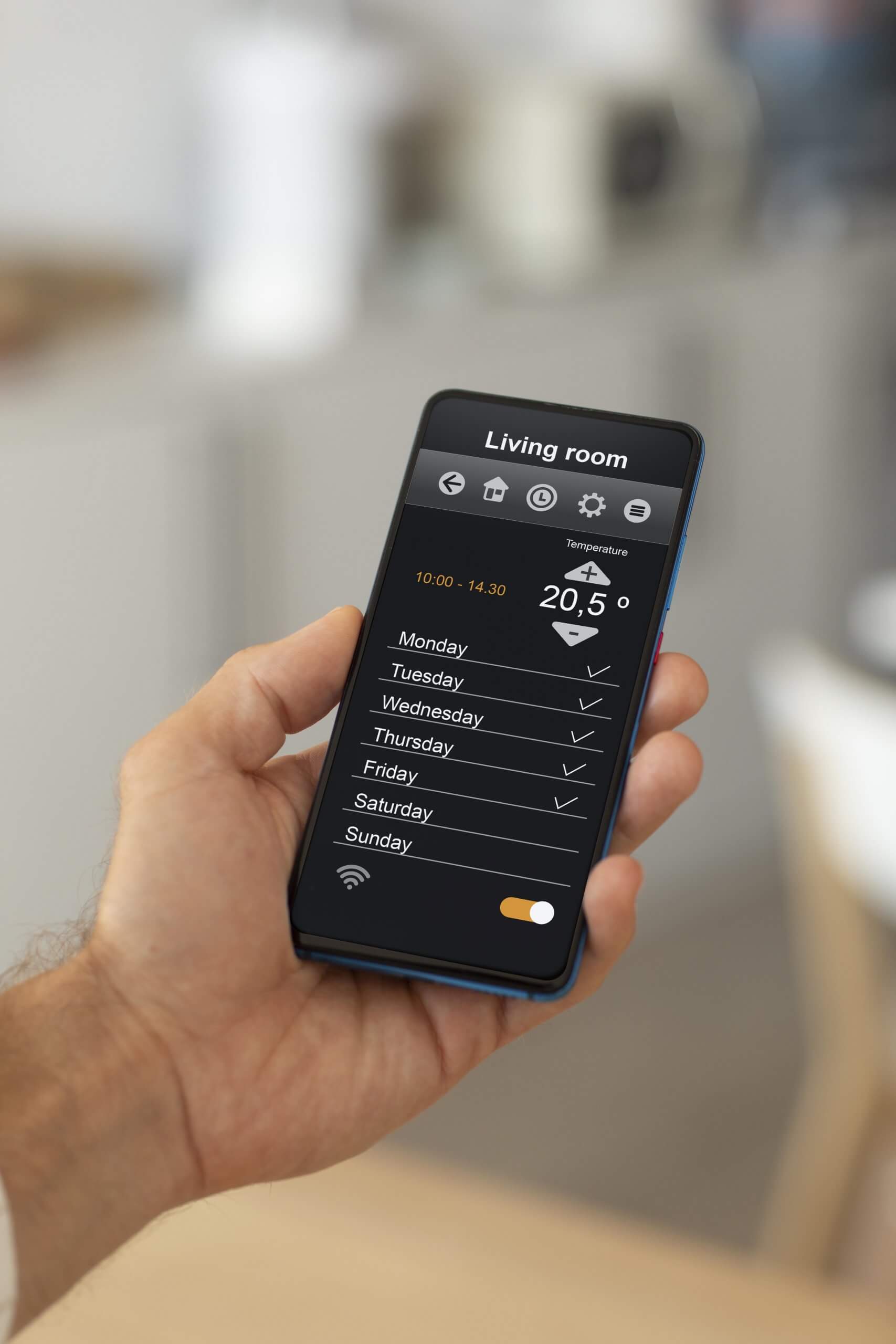 Eine Hand hält ein Smartphone mit geöffneter Kleiber GmbH App für Wohnraumlüftung, die Wochenpläne fürs Wohnzimmer zeigt
