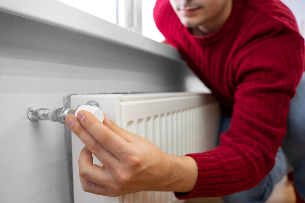 Eine Person im roten Pullover stellt das Thermostatventil an einem weißen Heizkörper ein, Entwurf einer automatisch gespeicherten Heizroutine