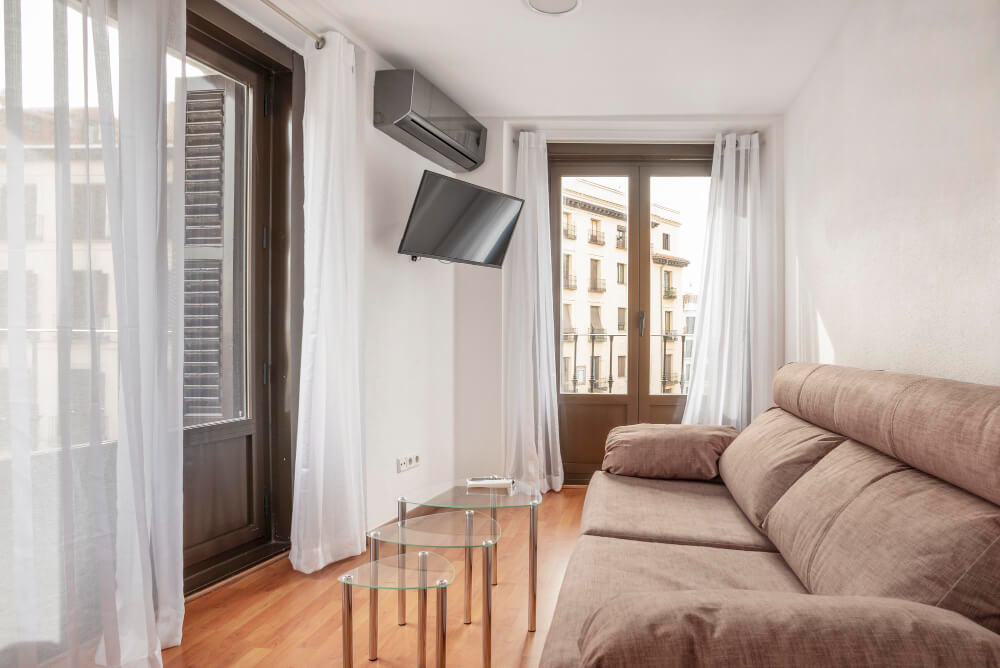 Helles Wohnzimmer im Neubau Ettlingen mit braunem Sofa, Glastischen, Parkettboden, großen Fenstern und gut gedämmter Wohnraumlüftung